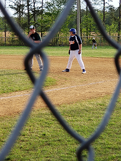 Photo taken through fence of two young boys on opposite teams playing baseball.