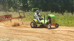 Man with helmet riding a modified lawnmower.